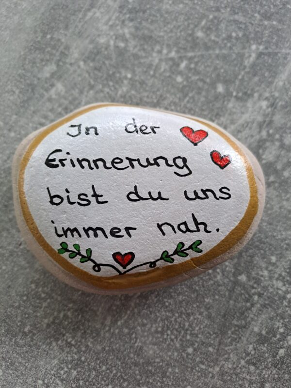 In der Erinnerung bist du uns immer nah Spruch Stein mit weißem Hintergrund, goldener Bordüre sowie kleinen Herzen und einer kleinen Blätterbordüre unten in der Mitte