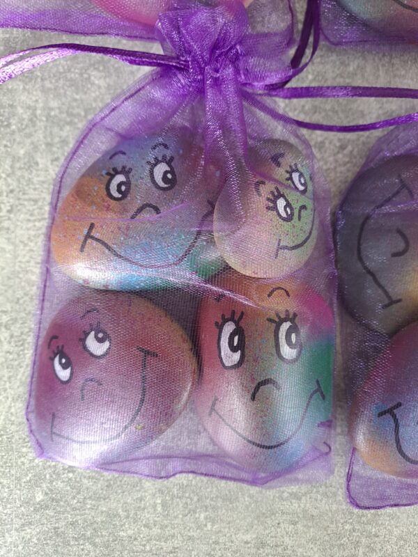 4er Set Schmunzelsteine, Viele kunterbunte Steine mit fröhlich lächelnden Gesichtern in einem lila Organzabeutel verpackt