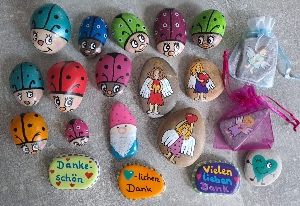 Auf dem Bild sind viele von mir bemalte Steine zu sehen, mehrere bunte Glückskäfer, Schutzengel, Dankesteine und ein Wichtel