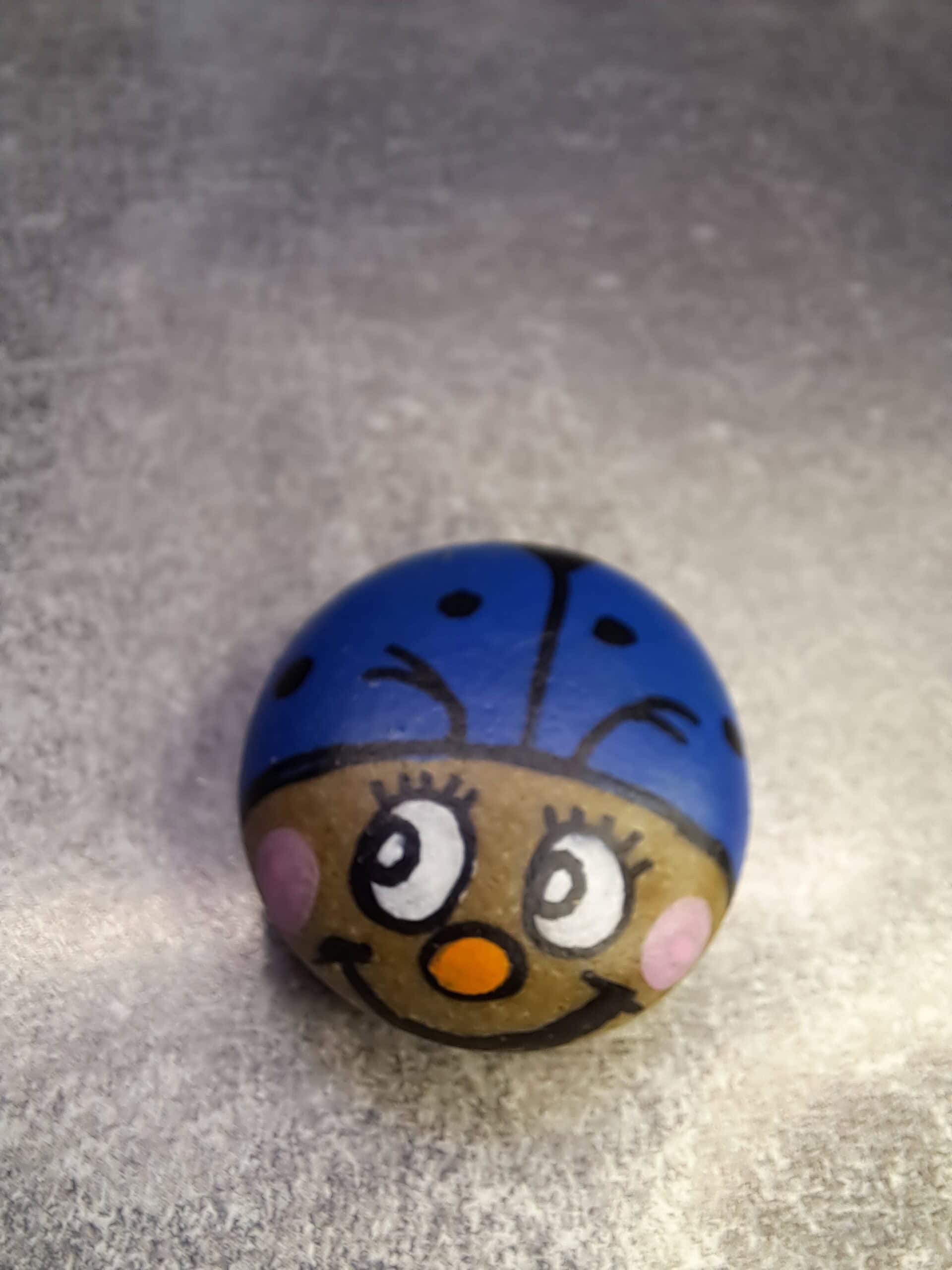 Stein bemalt als Blauer Glückskäfer Berti mit fröhlichem Gesicht