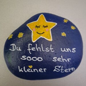 Du fehlst uns kleiner Stern, dunkelblauer Stein mit großem gelbem Stern und mehreren kleinen Sternchen und der weißen Aufschrift "Du fehlst und sooo sehr kleiner Stern"