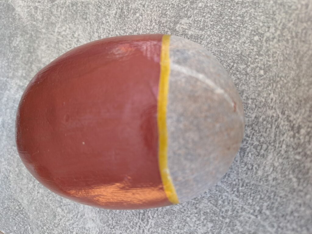 Maikäfer auf Stein malen, nächster Schritt, mit einem goldenen Stift eine dicke Linie entlang des Übergangs zwischen der braunen Farbe und dem unbemalten Teil des Steins malen 