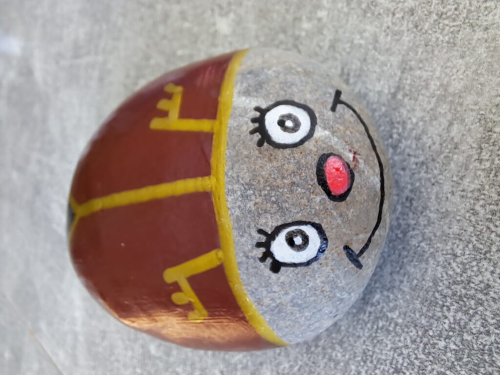 Maikäfer auf Stein malen, nun wird mit schwarz  ein Kringel ins Auge gemalt, bei dem innen ein weißer Punkt als Pupille frei bleibt