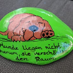 grüner Stein mit braunem schlafenden Hund und dem Spruch "Hunde liegen nicht faul herum, sie verschönern den Raum"