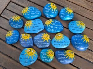 Sonnenstrahlen Spruchstein in verschiedenen Varianten, in verschiedenen Blautönen bemalte Steine mit einer lachenden Sonne darauf und einem schönen Spruch