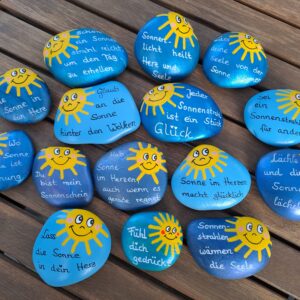 Sonnenstrahlen Spruchstein in verschiedenen Varianten, in verschiedenen Blautönen bemalte Steine mit einer lachenden Sonne darauf und einem schönen Spruch