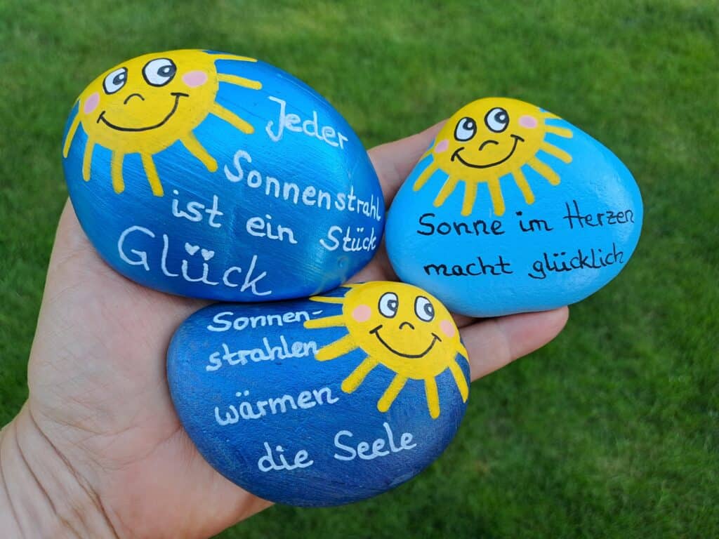 Verschenke Sonnenstrahlen, auf dem Bild ist eine Hand mit der der zur Auswahl stehenden Sonnensteine mit Spruch
