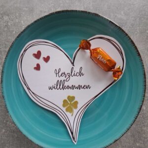 Herzensgruß Herzlich willkommen PDF-Druckvorlage ausgeschnitten auf türkisem Teller mit Praline