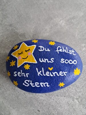 Dunkelblau lackierter Stein mit einem großen gelben Stern mit schlafendem Gesicht darauf, daneben viele kleine gelbe Steine und der Spruch Du fehlst uns sooo sehr kleiner Stern, Variante 4